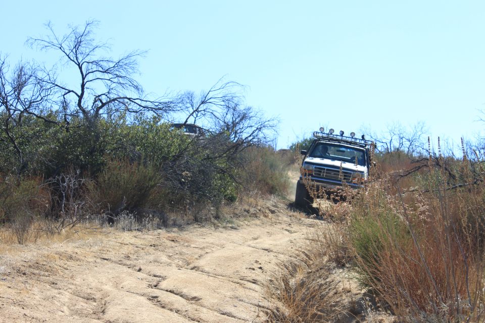White SUV with roof rack and lights driving on a dirt trail