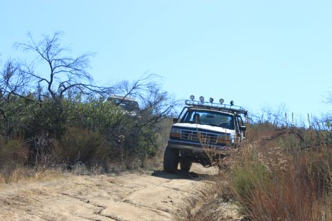 1992 Ford Bronco - Two trucks navigate a dry, dusty trail under a clear blue sky.