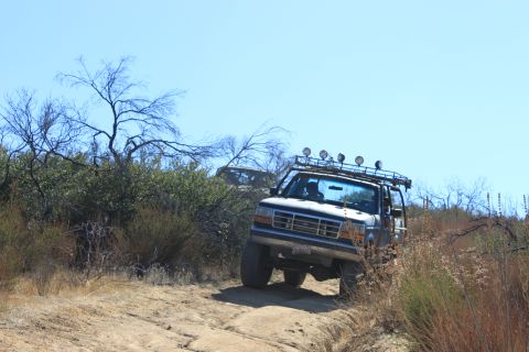 1992 Ford Bronco - Two off-road vehicles navigate a dusty trail under a clear blue sky.