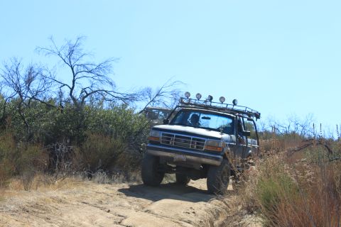 1992 Ford Bronco - A 1992 Ford Bronco navigates a dusty off-road path under a clear blue sky.