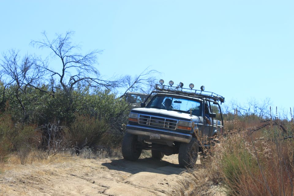 1992 Ford Bronco driving on a dirt trail with brush and trees
