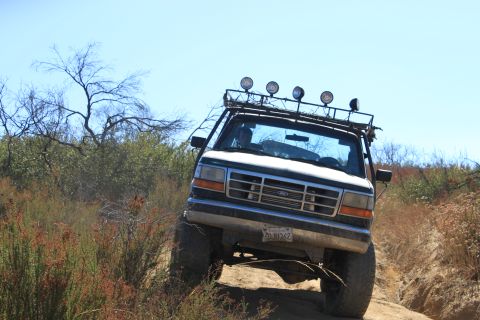 1992 Ford Bronco - A 1992 Ford Bronco navigates a dusty, off-road trail under a clear blue sky.