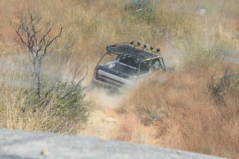 1992 Ford Bronco - A modified off-road vehicle navigates a dusty trail surrounded by dry vegetation.