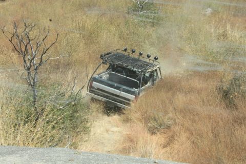 1992 Ford Bronco - An off-road vehicle navigates a dry, grassy terrain with a prominent roof rack.