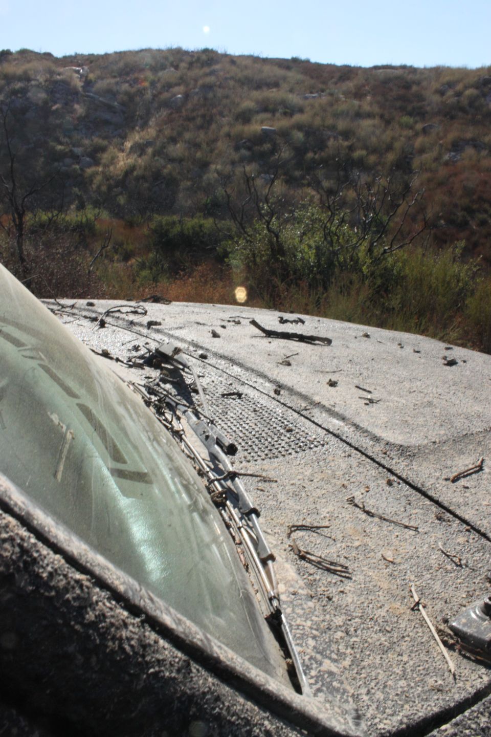 Dusty vehicle roof with debris and a partial windshield, angled view