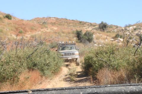 1992 Ford Bronco - A 1992 Ford Bronco navigates a dusty trail through dry brush and hills under a clear blue sky.