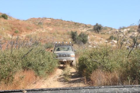 1992 Ford Bronco - 1992 Ford Bronco navigating an off-road trail surrounded by dry brush and hills.