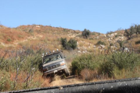 1992 Ford Bronco - 1992 Ford Bronco navigates a challenging off-road path through dry brush and hills.