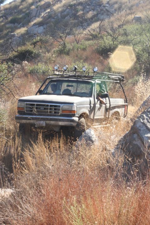 1992 Ford Bronco - 1992 Ford Bronco navigates a challenging off-road path through dry vegetation and rocks.