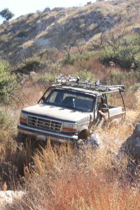 1992 Ford Bronco - A 1992 Ford Bronco navigates a dry, rocky trail with dense brush on either side.