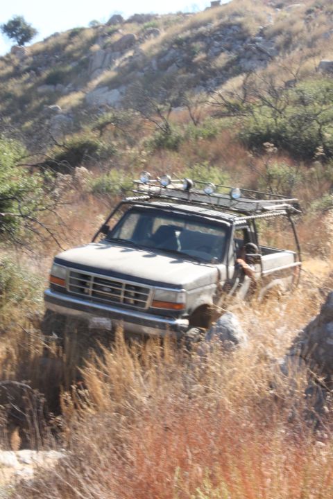1992 Ford Bronco - This 1992 Ford Bronco navigates a challenging, dry, and rocky terrain, equipped with a roof rack and auxiliary lights.