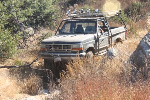1992 Ford Bronco - Off-road modified Ford F-Series truck navigating a rocky, overgrown trail.