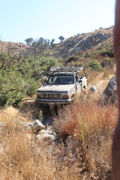 1992 Ford Bronco - A gray Ford F-Series truck navigates a , dry terrain, equipped with a roof rack for off-road adventures.