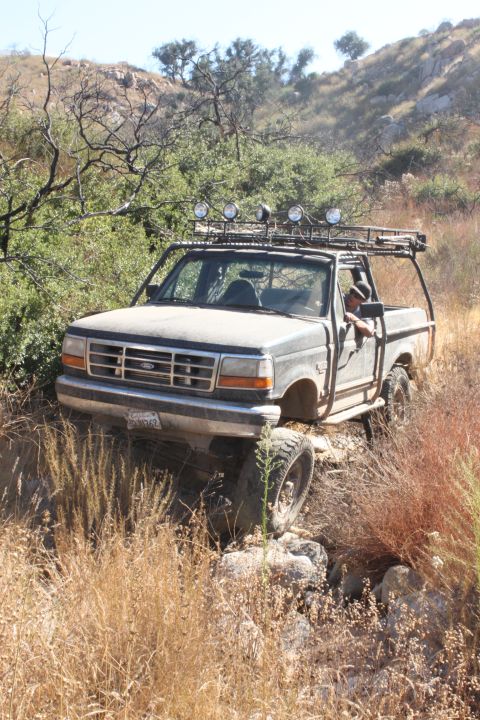 1992 Ford Bronco - This 1992 Ford Bronco navigates a , off-road trail, equipped with a roof rack and auxiliary lights.