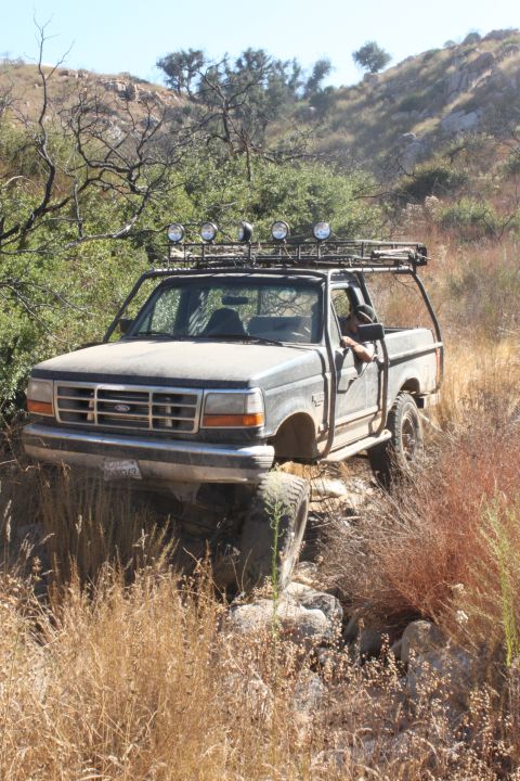 1992 Ford Bronco - 1992 Ford Bronco navigates a challenging rocky trail with a driver visible.