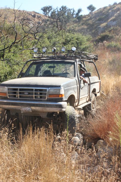 1992 Ford Bronco - This modified Ford truck is navigating a rocky, overgrown trail under a clear sky.