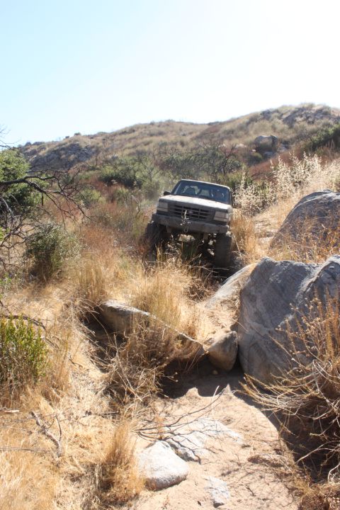 1992 Ford Bronco - 1992 Ford Bronco navigating a challenging off-road trail with large rocks and dry vegetation.