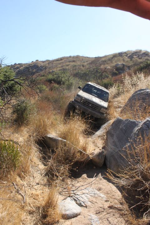 1992 Ford Bronco - A white off-road vehicle navigates a steep, rocky trail under a clear blue sky.