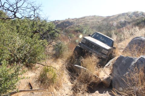 1992 Ford Bronco - This truck is navigating a challenging rocky trail with dry brush and trees.