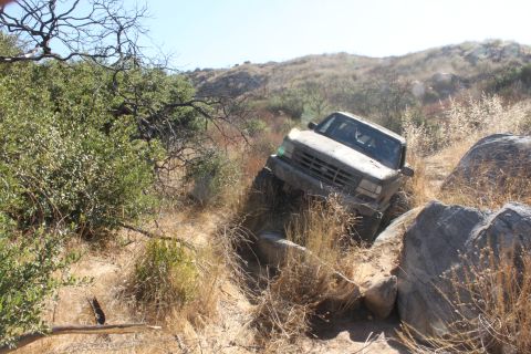 1992 Ford Bronco - A 1992 Ford Bronco maneuvers through a challenging, dry, rocky landscape with sparse vegetation.