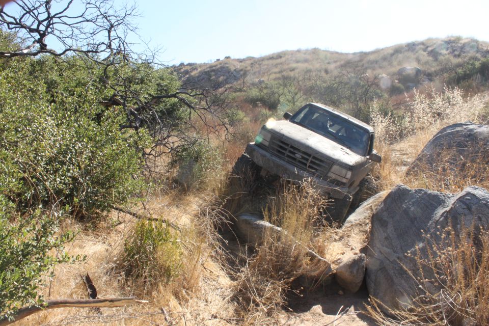 Gray 1992 Ford Bronco navigating rocky terrain, front-right wheel high