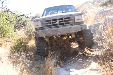 1992 Ford Bronco - A 1992 Ford Bronco navigates a rocky, off-road path with dry vegetation.