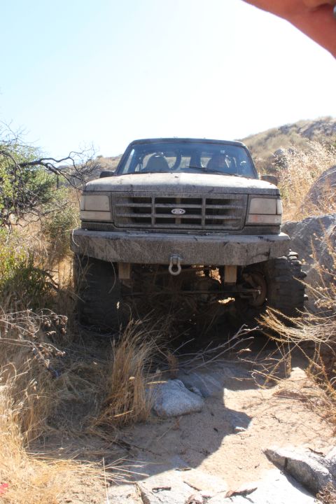 1992 Ford Bronco - A 1992 Ford Bronco navigates a rocky, off-road path with a clear blue sky overhead.