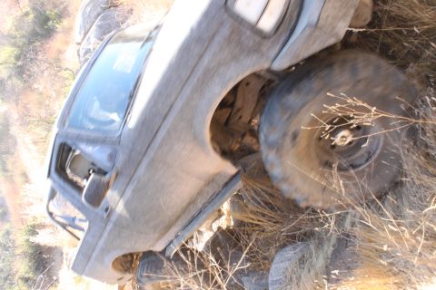 1992 Ford Bronco - A gray SUV is partially overturned on a rocky, grassy incline, with its front wheel prominently displayed.
