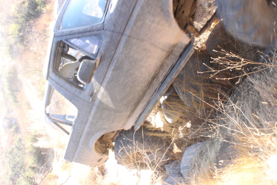 Mud-covered off-road vehicle with roll cage, parked on rocky terrain