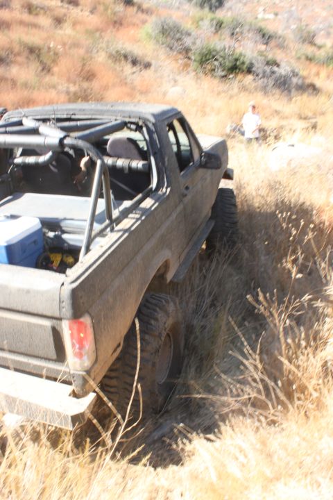 1992 Ford Bronco - A modified 1992 Ford Bronco navigates a dry, grassy hillside with a person visible in the background.