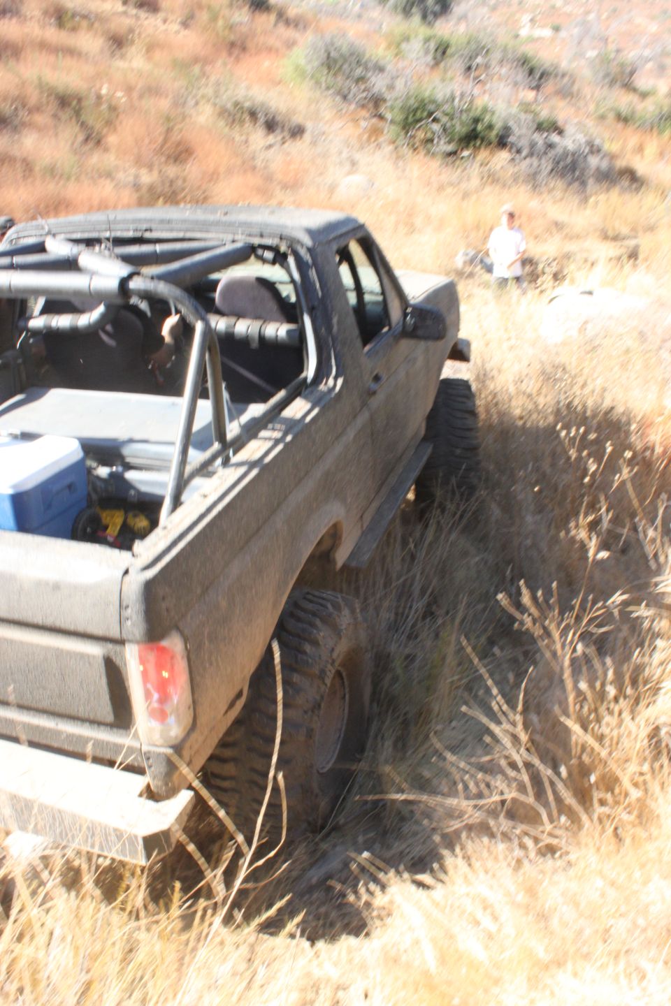 Dark gray 1992 Ford Bronco with roll cage, off-road tires, and cooler in the bed, angled from the rear quarter
