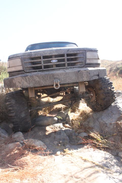1992 Ford Bronco - A 1992 Ford Bronco navigates a rocky off-road trail, its front end covered in mud.