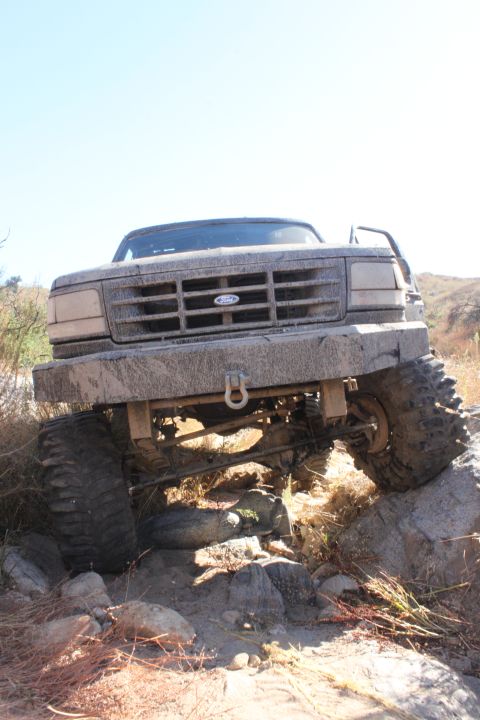 1992 Ford Bronco - Mud-covered 1992 Ford Bronco navigating a rocky off-road trail.