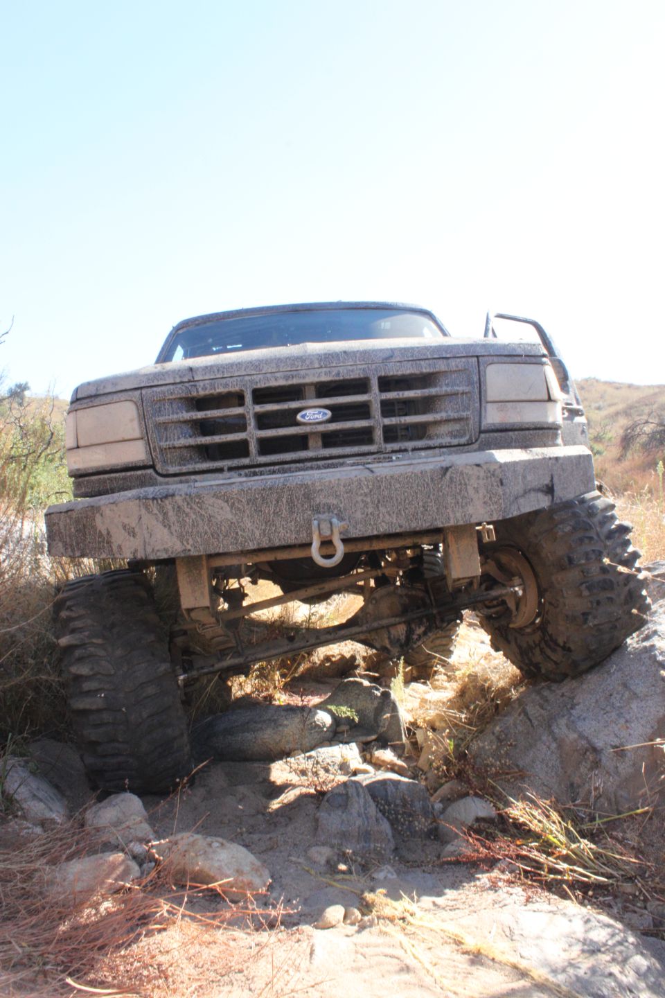 1992 Ford Bronco front end tilted on rocks, covered in mud