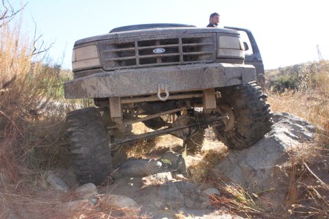 1992 Ford Bronco - A 1992 Ford Bronco navigates a rocky trail, its front end tilted upwards as it climbs over an obstacle.