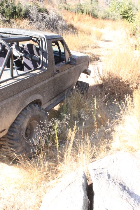 1992 Ford Bronco - Mud-covered 1992 Ford Bronco navigates a rough, off-road path.