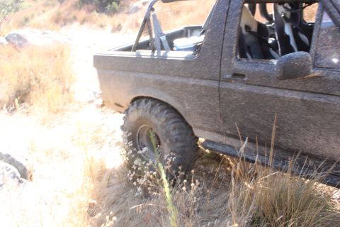1992 Ford Bronco - A muddy 1992 Ford Bronco is shown from the side, equipped for off-road driving with large tires and racing seats.