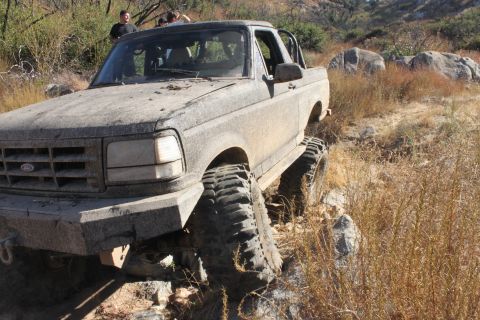 1992 Ford Bronco - A 1992 Ford Bronco is shown off-roading on a dry, rocky trail with dense brush.