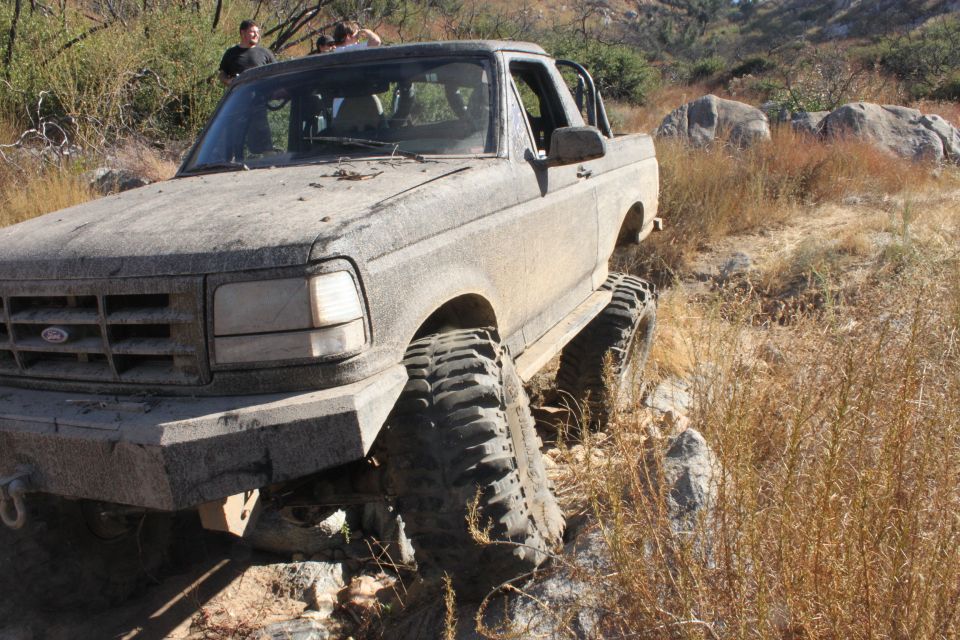 Mud-covered 1992 Ford Bronco with large off-road tires navigating rocky terrain