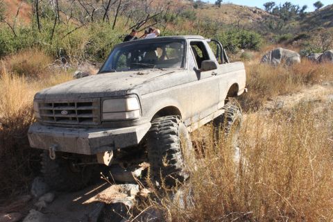 1992 Ford Bronco - This 1992 Ford Bronco navigates a challenging off-road trail, its ruggedness evident through the mud and terrain.