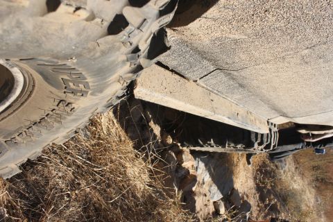 1992 Ford Bronco - A close-up view of a tire and the undercarriage of a vehicle, with dry grass and dirt visible.
