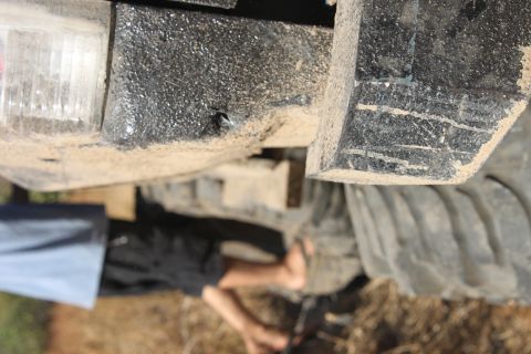 1992 Ford Bronco - A close-up view of a vehicle's dirty undercarriage and tire, with a person's legs visible below.