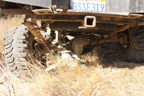 1992 Ford Bronco - The underside of a truck, showing its heavy-duty suspension and large off-road tires, parked in a dry, grassy area.