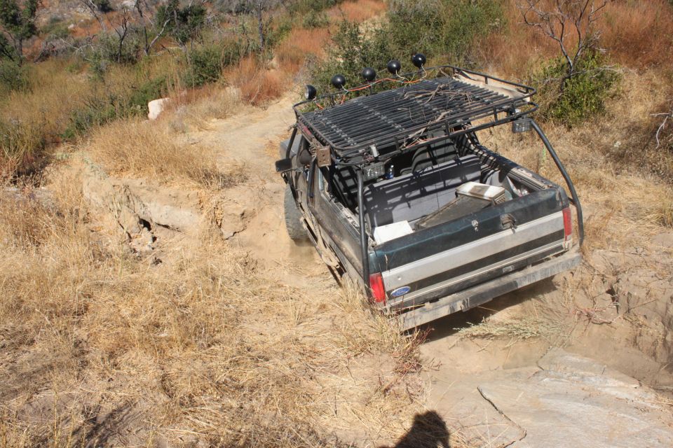 1992 Ford Bronco with roof rack driving on a dry, rutted dirt trail