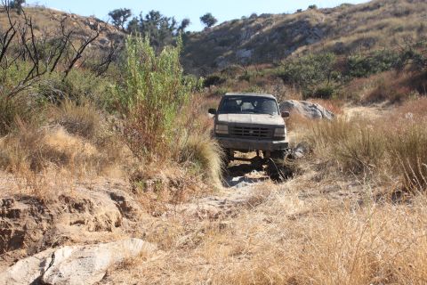 1992 Ford Bronco - A 1992 Ford Bronco navigates a rough, dry trail surrounded by arid vegetation and rocky terrain.
