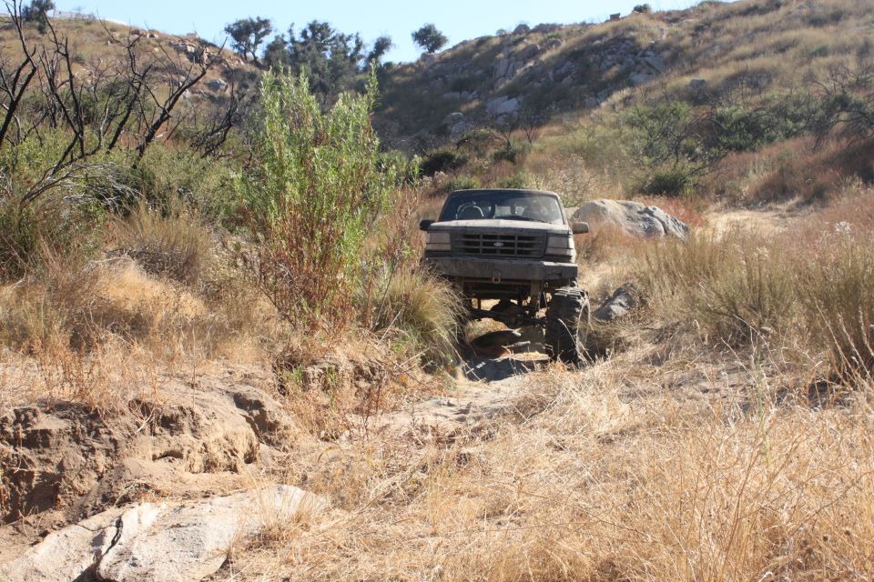 1992 Ford Bronco on a rocky trail, front view. Muddy, lifted, with large tires