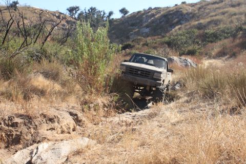 1992 Ford Bronco - A gray 1992 Ford F-150 pickup truck navigates a challenging off-road trail with dry brush and rocks.