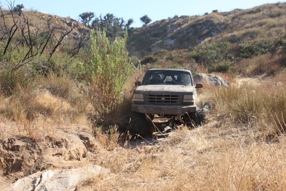 Ford truck navigating a dry, rocky trail with brush and hills in the background