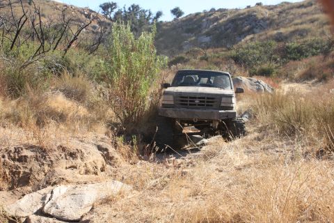 1992 Ford Bronco - A gray Ford F-Series truck navigates a challenging, dry, and rocky off-road trail.