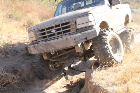 1992 Ford Bronco - A lifted Ford Bronco navigates a rocky off-road course, kicking up dust.